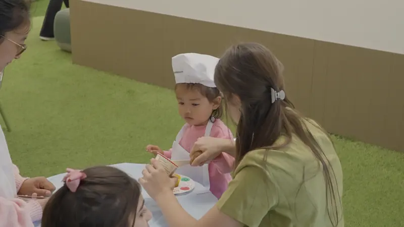 An educator and a child in a chef's hat baking together